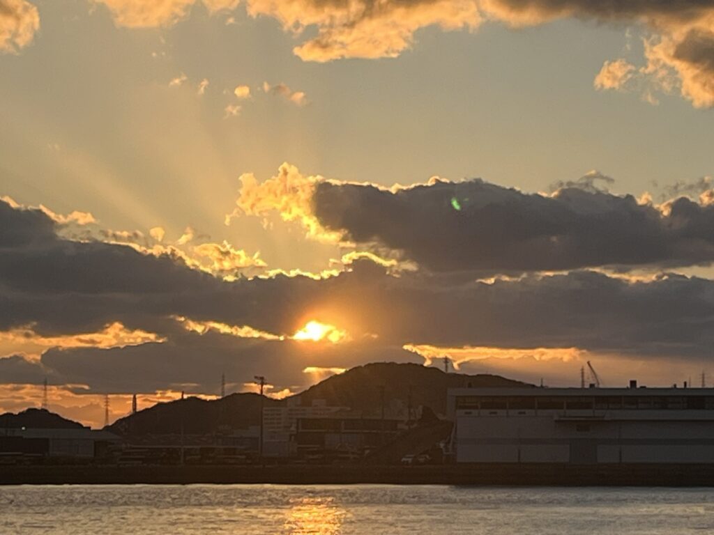 太陽が赤く輝き雲間から光が漏れている風景
